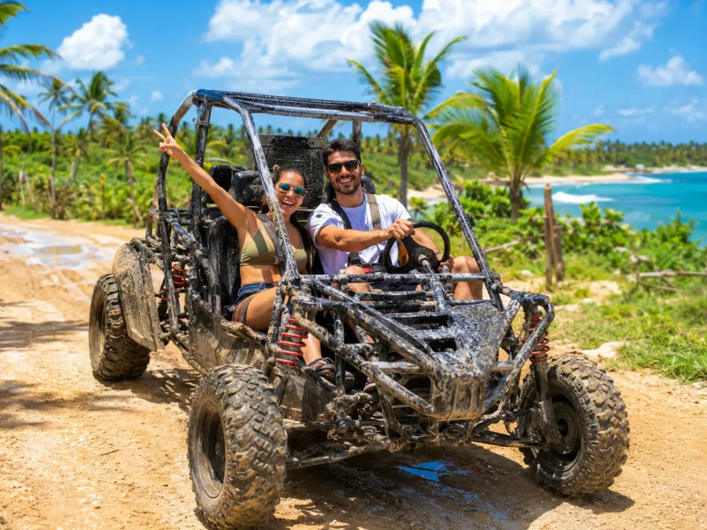 Couple enjoying a muddy buggy tour in Punta Cana on a tropical trail near palm trees, countryside views, and the Caribbean coast.
