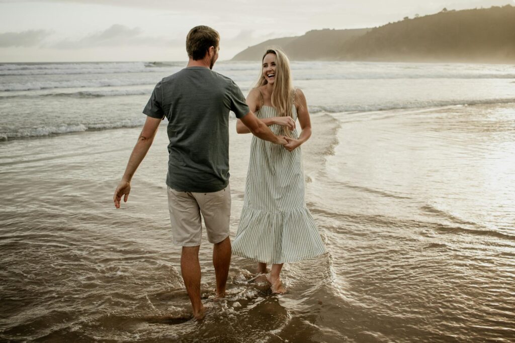 A couple joyfully walking hand in hand along the beach, with waves gently lapping at their feet during sunset.