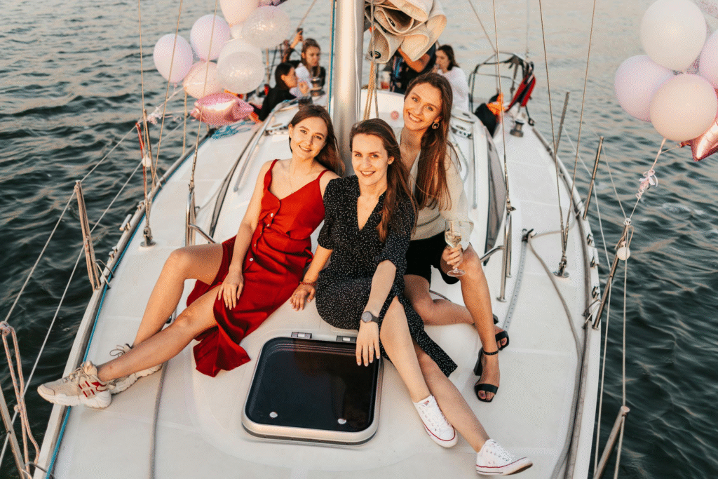 Three friends enjoying a cheerful moment on a sailboat, celebrating with drinks and balloons.