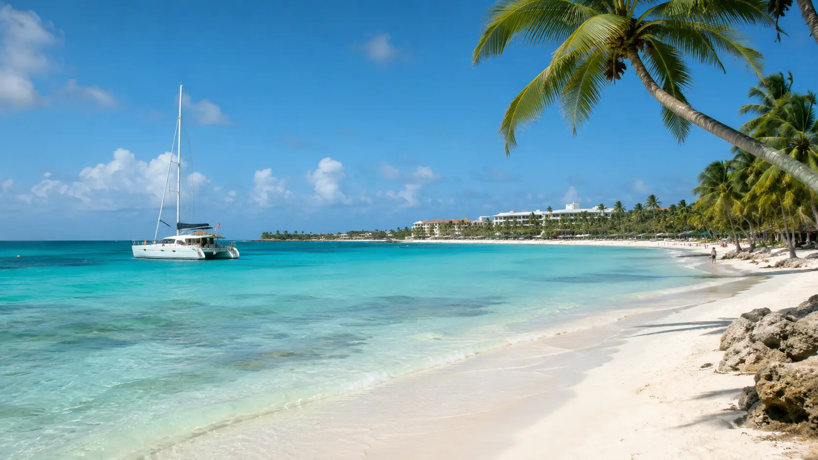 Peaceful Punta Cana beach with turquoise water, palm trees, resort coastline, and a catamaran sailing near shore