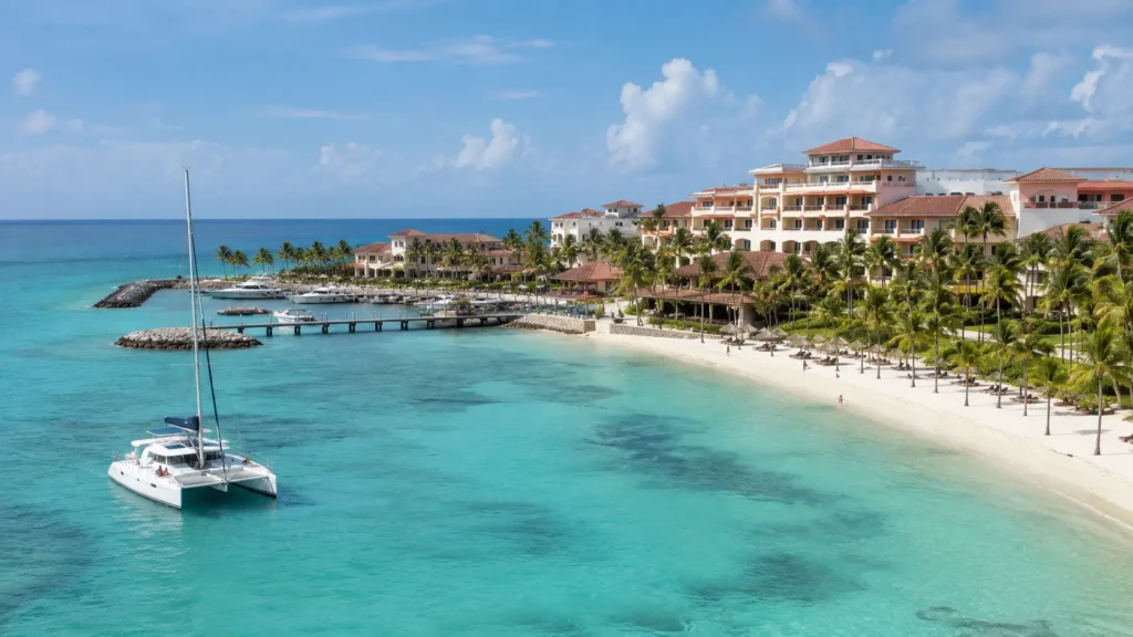 Punta Cana resort coastline with turquoise water, palm trees, marina docks, and a catamaran near the beach