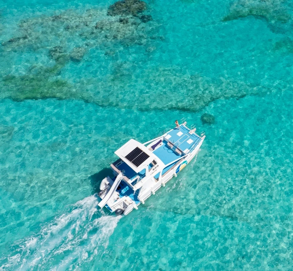 Aerial view of a catamaran cruising over crystal-clear turquoise water and coral reefs in Punta Cana, showcasing a scenic Caribbean snorkeling and island adventure.