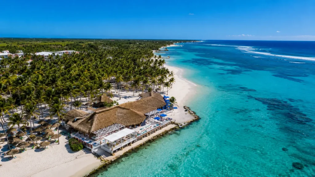Aerial view of a luxury Punta Cana beachfront resort with crystal-clear Caribbean water, white sand beach, tropical palm trees, and oceanfront accommodations in the Dominican Republic.