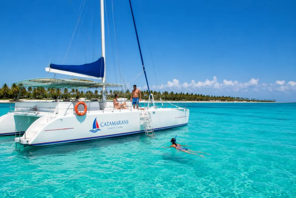 White catamaran on turquoise water in Punta Cana with guests relaxing near a palm lined beach