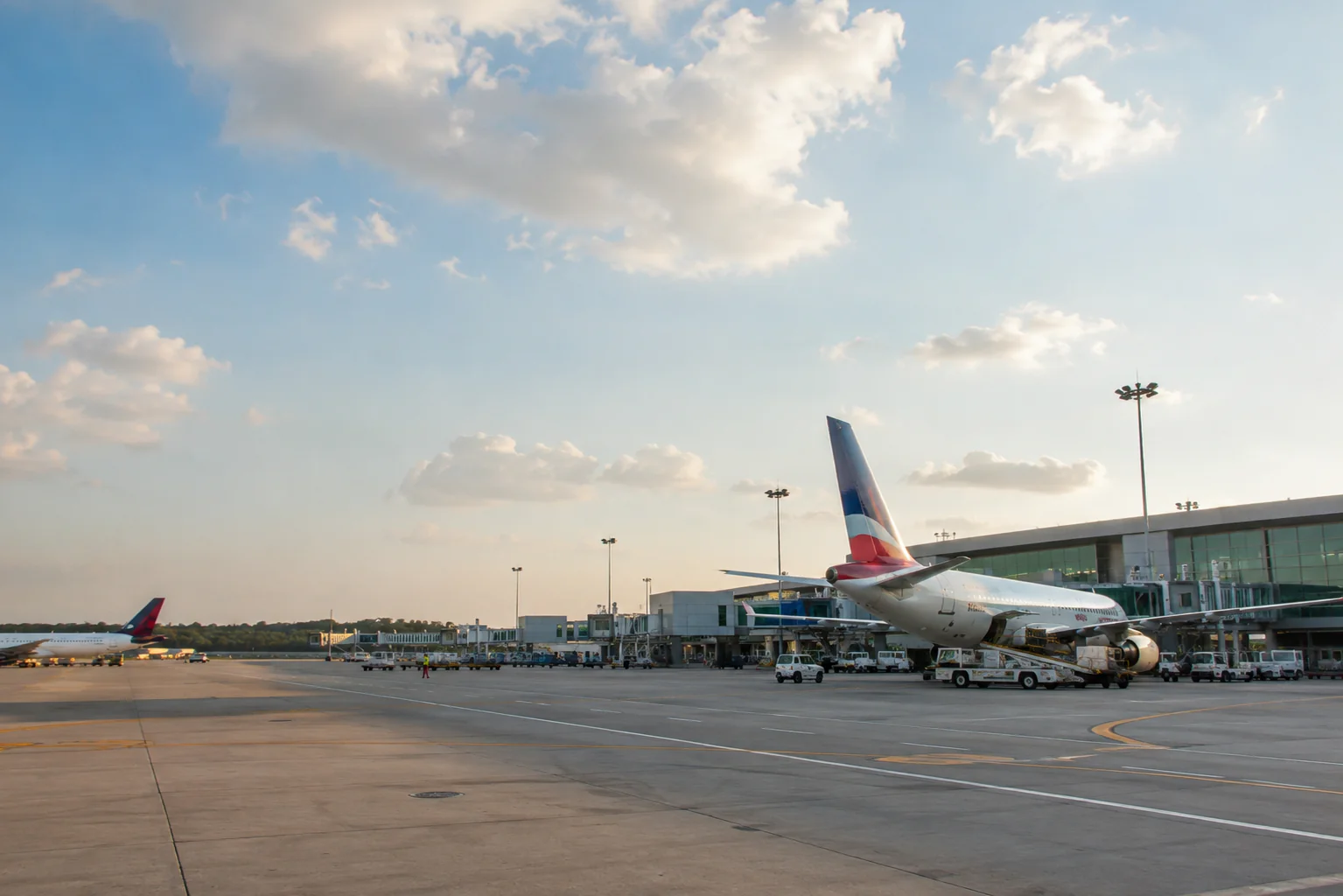 Commercial airplanes parked on the runway at Punta Cana Airport with the terminal building under a bright sky, showing an international airport arrival scene in the Dominican Republic.